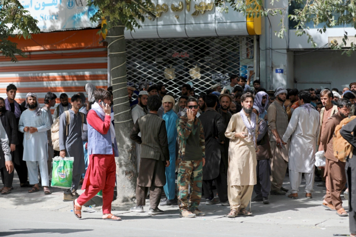 Afghans wait in long lines for hours to withdraw money in front of a bank in Kabul. [Rahmat Gul/AP Photo]